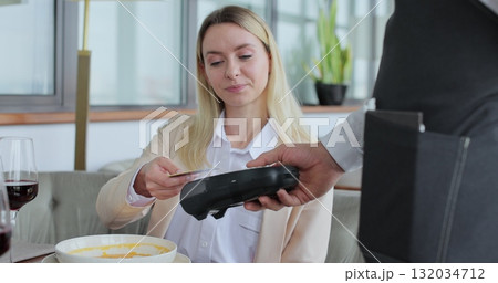 Woman paying restaurant bill using smartphone. Waiter giving terminal for cashless payment to woman. Technology device concept. Woman paying restaurant bill using smartphone. Waiter giving terminal for cashless payment to woman. Technology device concept. 132034712