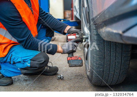 Mechanic using an impact wrench to remove lug nuts from a car wheel. Seasonal tire change and professional car service in preparation for winter. Mechanic using an impact wrench to remove lug nuts from a car wheel. Seasonal tire change and professional car service in preparation for winter. 132034764