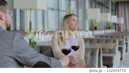 Waiter carries two glasses of wine to a young couple at a table in a restaurant. Waiter carries two glasses of wine to a young couple at a table in a restaurant. 132034778