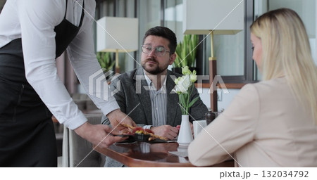Waiter brings order for couples in restaurant. Couple sitting by table in a cafe. Customer service. 132034792