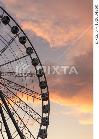 large Ferris wheel against a cloudy sky. The Ferris wheel is surrounded by sunset clouds. 132034960