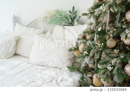 Cozy bedroom corner decorated for holidays with festive Christmas tree and bed with white bedding 132035084