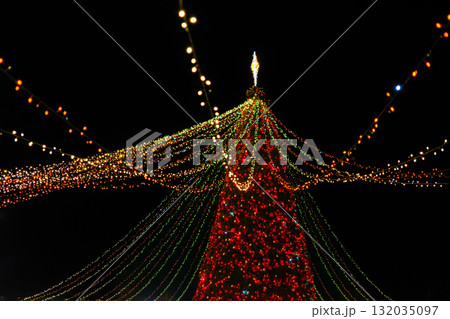 Giant Christmas tree with festive lights and glowing decorations at night fair, holiday celebration Giant Christmas tree with festive lights and glowing decorations at night fair, holiday celebration 132035097