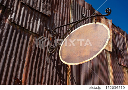 Blank metal antique shop sign. Oval shape vintage signboard with empty space hanging on wrought iron 132036210