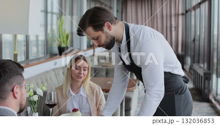 Waiter and coffee on a tray, walking to a customer in or restaurant cafe. Man and woman talking together and enjoying evening. Waiter and coffee on a tray, walking to a customer in or restaurant cafe. Man and woman talking together and enjoying evening. 132036853