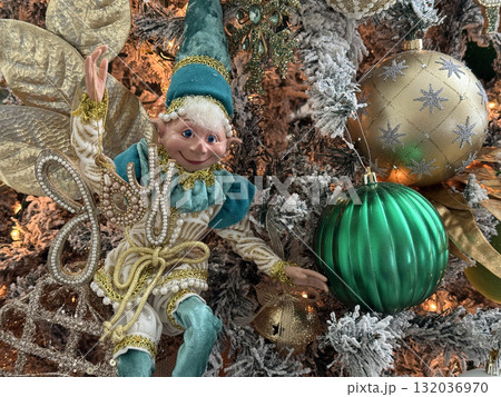 A cheerful elf doll in turquoise and gold sits among glittering Christmas ornaments. The detailed decor captures a playful and elegant festive spirit. 132036970