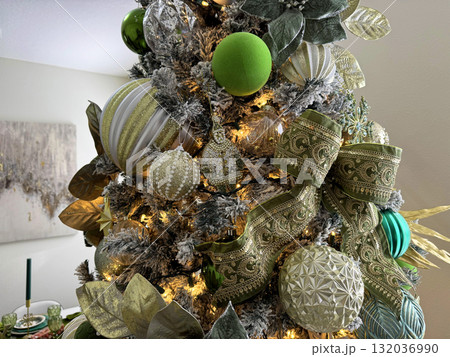 A detailed view of a Christmas tree with elegant ornaments, leaves, and a large green ribbon bow. The gold and silver decorations shine under warm holiday lights. 132036990