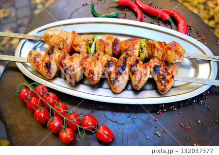 grilled chicken skewers glistening with marinade, displayed in a stainless steel tray, showcasing appetizing barbecue cuisine. 132037377
