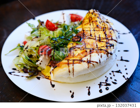white omelet with salad on a plate, drizzled with sauce 132037431