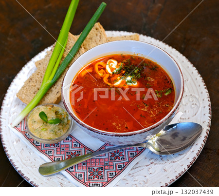 borsch with green onions on an embroidered napkin with a spoon and garlic spread sauce for bread 132037439