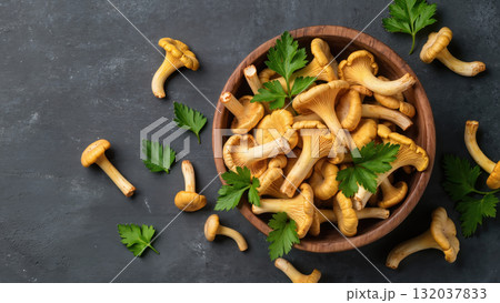 Fresh chanterelle mushrooms in wooden bowl with parsley leaves on dark background. Top view of seasonal edible fungi. Natural organic food ingredient. 132037833