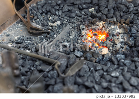Close-up detail old medieval blacksmith furnace with hot burning coal flame forge iron metal. Craft smith farrier workshop fireplace with many professional craftsman tools equipment 132037992