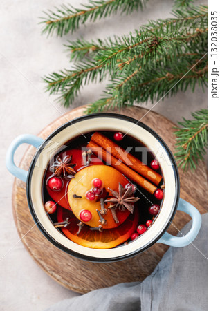 A pot of red mulled wine with spices, orange, apple slices, and cranberries on a wooden board 132038035
