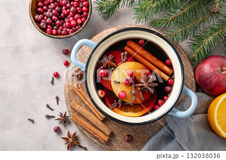 A pot of red mulled wine with spices, orange, apple slices, and cranberries on a wooden board 132038036