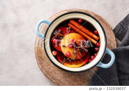 A pot of red mulled wine with spices, orange, apple slices, and cranberries on a wooden board 132038037