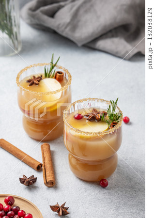 Two glasses of hot apple cider with cinnamon, anise, brown sugar and rosemary on a light background 132038129