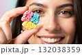 Close-up of a smiling woman holding a colorful piece of porous candy. Selective focus on the unique texture of a sweet snack Close-up of a smiling woman holding a colorful piece of porous candy. Selective focus on the unique texture of a sweet snack 132038359