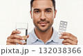 A man holds a blister pack of pills and a glass of water for medical treatment. Close-up portrait of a person taking daily medication. Healthcare and wellness concept on a white background A man holds a blister pack of pills and a glass of water for medical treatment. Close-up portrait of a person taking daily medication. Healthcare and wellness concept on a white background 132038366