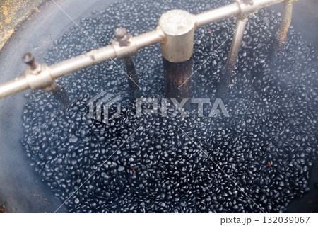 Coffee roasting process in a traditional setup with dark roasted beans in a large roasting machine surrounded by smoke 132039067