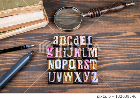 Alphabet concept with colorful wooden block letters arranged on wooden desk alongside books 132039346