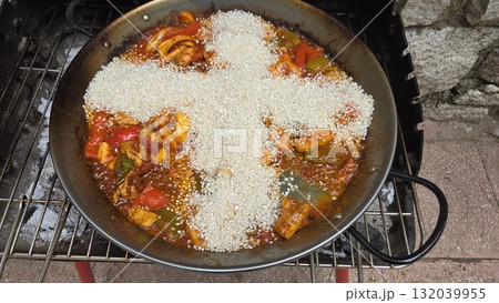 Traditional spanish paella preparation with vibrant vegetables and rice in a pan. Rice in the shape of a cross in paella. Typical cuisine of Spain. Stage of cooking paella. Ingredients for paella 132039955