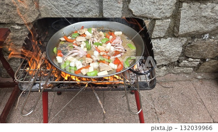 Traditional spanish paella cooking outdoors with seafood and vegetables. Typical cuisine of Spain. Valencian cuisine. Stage of cooking paella. Ingredients for paella 132039966