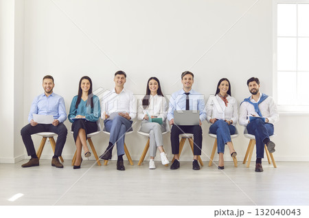 A group of smiling colleagues sitting in a row in an empty room 132040043