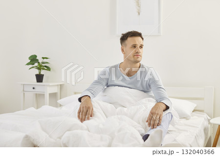 Man in pajamas wakes up in morning with slightly tired expression, probably due to restless sleep. Man in pajamas wakes up in morning with slightly tired expression, probably due to restless sleep. 132040366