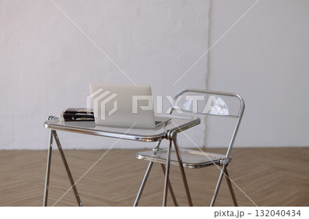 Minimalist chrome desk and transparent chair with laptop on wooden floor against white wall Minimalist chrome desk and transparent chair with laptop on wooden floor against white wall 132040434