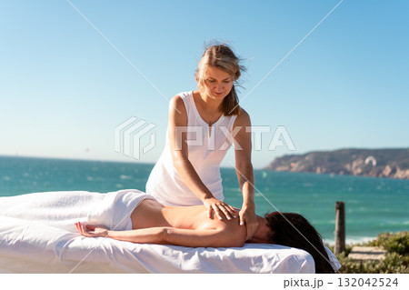 Masseur giving back massage to woman near sea at Masseur giving back massage to woman near sea at 132042524