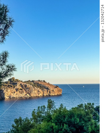 Scenic landscape of rocky seaside cliff surrounded by deep blue ocean water with a sailboat on horizon, representing travel, freedom, and nature. High quality photo Scenic landscape of rocky seaside cliff surrounded by deep blue ocean water with a sailboat on horizon, representing travel, freedom, and nature. High quality photo 132042714