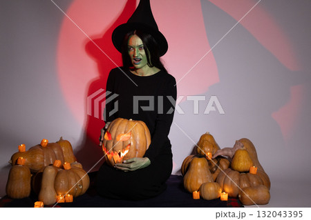 Woman in black dress holding pumpkin in front of spooky decor Woman in black dress holding pumpkin in front of spooky decor 132043395