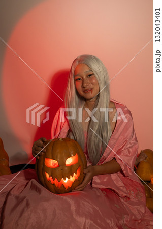 Woman in pink dress holding a pumpkin amidst a colorful autumn garden 132043401