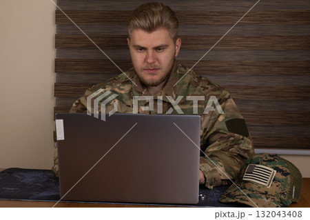 Man in military uniform using laptop in a bustling airport terminal 132043408