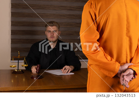 A man in an orange prison uniform sits quietly, staring out of the cell bars  132043513
