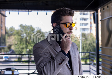 Man in coat and sunglasses talking on cell phone in urban street setting 132043528