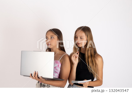 Two young women are looking at something off-camera, with one holding a laptop. 132043547