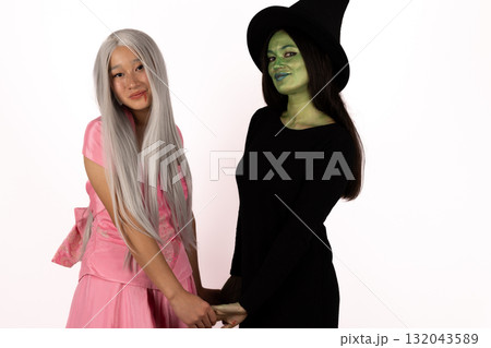 The two women, one dressed as a witch are standing side-by-side and holding hand The two women, one dressed as a witch are standing side-by-side and holding hand 132043589