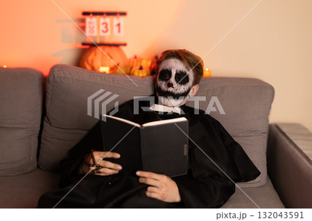 A man in a skeleton mask reading a book 132043591