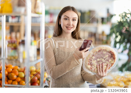 In shop girl scans QR code and take reading on pizza with prosciutto filling using phone camera 132043901