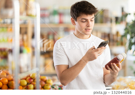 Young man customer at shop scans QR code on smoothie package using phone camera Young man customer at shop scans QR code on smoothie package using phone camera 132044016