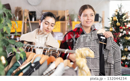 Two happy friends choosing coat or jacket in clothing store Two happy friends choosing coat or jacket in clothing store 132044234