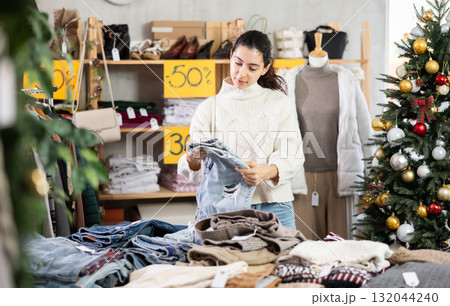 Uncertain young Armenian girl choosing jeans pantaloons in clothing store 132044240