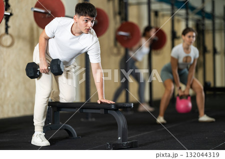 Young guy training with dumbbells on bench Young guy training with dumbbells on bench 132044319