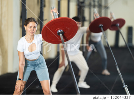 Young woman training with barbell with one arm 132044327