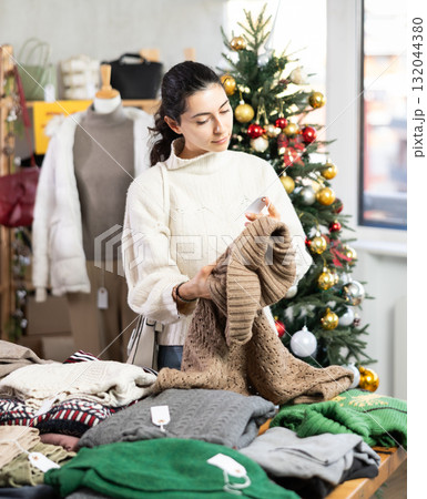 Uncertain young Armenian girl choosing sweater in clothing store 132044380