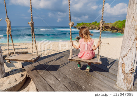 Child girl on swings at beach with blue sea, enjoy childhood 132047089