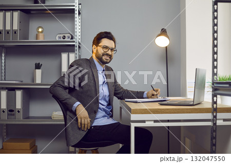 Young business man working at the desk on his workplace at office, looking at the camera smiling. 132047550