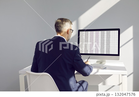 Businessman or accountant at workplace compares data on electronic spreadsheet on computer. Businessman or accountant at workplace compares data on electronic spreadsheet on computer. 132047576