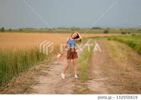 Young woman enjoying a sunny day in a wheat field while posing along a dirt road Young woman enjoying a sunny day in a wheat field while posing along a dirt road 132050819